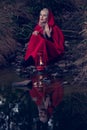 Attractive woman dressed a little red riding-hood cross stream in a dark forest with a lantern Royalty Free Stock Photo