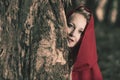 Attractive woman dressed a little red riding-hood hide behind a tree in dark forest Royalty Free Stock Photo