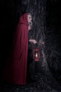 Attractive woman dressed a little red riding-hood walk in a dark forest with lantern Royalty Free Stock Photo