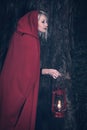 Attractive woman dressed a little red riding-hood walk in a dark forest with lantern Royalty Free Stock Photo