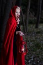 Attractive woman dressed a little red riding-hood walk in a dark forest with lantern Royalty Free Stock Photo