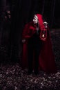 Attractive woman dressed a little red riding-hood walk in a dark forest with lantern Royalty Free Stock Photo