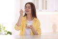 Attractive woman eating tasty yogurt at table in kitchen Royalty Free Stock Photo