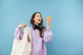 Attractive woman with an eco bag in her hands stands on a blue background with an apple in her hand and looks at the fruit with a Royalty Free Stock Photo