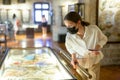 Woman in mask looking at the exposition of antique hand fan at museum