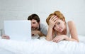 attractive woman feeling upset unsatisfied and frustrated in bed with his husband while the man work on computer laptop ignoring h Royalty Free Stock Photo