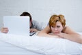 attractive woman feeling upset unsatisfied and frustrated in bed with his husband while the man work on computer laptop ignoring h Royalty Free Stock Photo