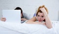 attractive woman feeling upset unsatisfied and frustrated in bed with his husband while the man work on computer laptop ignoring h Royalty Free Stock Photo