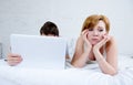 attractive woman feeling upset unsatisfied and frustrated in bed with his husband while the man work on computer laptop ignoring h