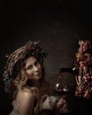 Attractive woman with glass of red wine in wine cellar . Vine wreath with blue grapes on a head. Red wine is poured from a bottle Royalty Free Stock Photo