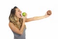 Attractive woman holding apple and chocolate donut in healthy fruit versus sweet junk food temptation