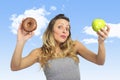 Attractive woman holding apple and chocolate donut in healthy fruit versus sweet junk food temptation Royalty Free Stock Photo