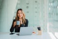 Attractive woman holding coffee cup and using laptop while sitting at her workplace Royalty Free Stock Photo