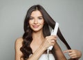 Attractive woman holding hair iron and straightening her healthy long dark hair on white background. Haircare and hair styling Royalty Free Stock Photo