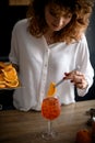 Attractive woman holds tweezers with slice of orange over glass with drink.