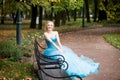 Attractive woman in long blue dress sitting in bench in park Royalty Free Stock Photo