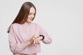 Attractive woman looks at smartwatch, checks calories or pulse, wears casual oversized sweater, has dark staight hair, on