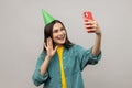 Attractive woman with party cone making selfie or broadcasting livestream, waving hand, saying hello