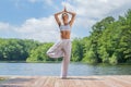 Attractive woman is practicing yoga, doing Vrksasana exercise, standing in tree pose near lake Royalty Free Stock Photo