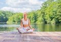 Attractive woman is practicing yoga and meditation, sitting in lotus pose near lake in morning Royalty Free Stock Photo