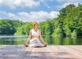 Attractive woman is practicing yoga sitting in Gomukasana exercise near lake. Young woman is meditating in Cow Face pose outdoors
