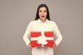 Attractive woman with present box posing with surprised face expression on gray background. Girl holding gift decorated Royalty Free Stock Photo