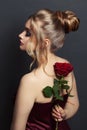 Attractive woman profile and back head with blonde hair updo hairdo and red rose flower on black Royalty Free Stock Photo