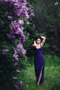 Attractive woman in purple dress posing near lilac flowering bushes