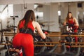 Attractive woman in a red sports suit in gym, riding on speed stationary bike. Rear view. Reflection in the mirror Royalty Free Stock Photo