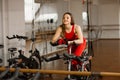 Attractive woman in a red sports suit in gym, riding on speed stationary bike. Reflection in the mirror Royalty Free Stock Photo