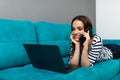 Attractive woman relaxing on sofa with laptop talking on phone. Smiling young woman speaking by mobile lying on couch at home Royalty Free Stock Photo