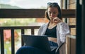 Attractive woman sits with a laptop on the balcony and works, looking intently at the screen. Beautiful girl freelancer in casual Royalty Free Stock Photo