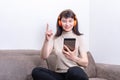 Attractive woman sitting on the couch in orange headphones talking to the tablet and raising her finger up Royalty Free Stock Photo