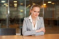 Attractive woman sitting at desk in meeting room looking friendly to the camera against blurred glass wall Royalty Free Stock Photo