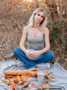 Attractive woman sitting on a plaid with drink and bakery on a picnic in forest with warm sunshine Royalty Free Stock Photo