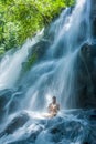 Attractive woman sitting at rock in yoga pose for spiritual relaxation serenity and meditation at stunning beautiful waterfall and Royalty Free Stock Photo