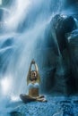 Attractive woman sitting at rock in yoga pose for spiritual relaxation serenity and meditation at stunning beautiful waterfall and Royalty Free Stock Photo
