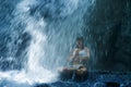 Attractive woman sitting at rock in yoga pose for spiritual relaxation serenity and meditation at stunning beautiful waterfall and Royalty Free Stock Photo