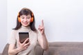 Attractive woman sitting on a sofa wearing orange headphones looking into a tablet and raising her finger up Royalty Free Stock Photo