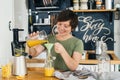 Attractive woman with a smile in her kitchen in a rustic style, makes fresh orange juice from a orange bottle by pouring it into a Royalty Free Stock Photo