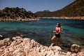 attractive woman stands on rocky coast of sea against background of hills and sky