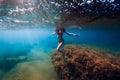 Attractive woman stay at stone with seaweed in underwater. Swimming in blue sea