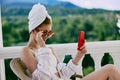 Attractive woman in sunglasses sits on the balcony and uses the phone unaltered Royalty Free Stock Photo