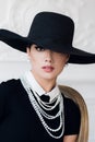 Attractive woman wearing black dress, hat and pearls, sitting on chair Royalty Free Stock Photo