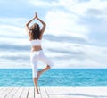 Attractive woman in white sporty clothes doing yoga on a wooden pier. Yoga, sport, leisure, recreation and freedom. Royalty Free Stock Photo