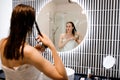 Attractive woman in white towel with comb brushing her wet hair after showering at home in front of bathroom mirror. Cares about Royalty Free Stock Photo