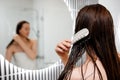 Attractive woman in white towel with comb brushing her wet hair after showering at home in front of bathroom mirror. Cares about Royalty Free Stock Photo