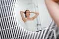 Attractive woman in white towel with comb brushing her wet hair after showering at home in front of bathroom mirror. Cares about Royalty Free Stock Photo