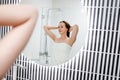 Attractive woman in white towel with comb brushing her wet hair after showering at home in front of bathroom mirror. Cares about Royalty Free Stock Photo