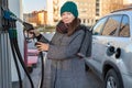 Attractive woman in winter clothing taking gas nozzle for car refueling, petrol station, person looking at camera Royalty Free Stock Photo